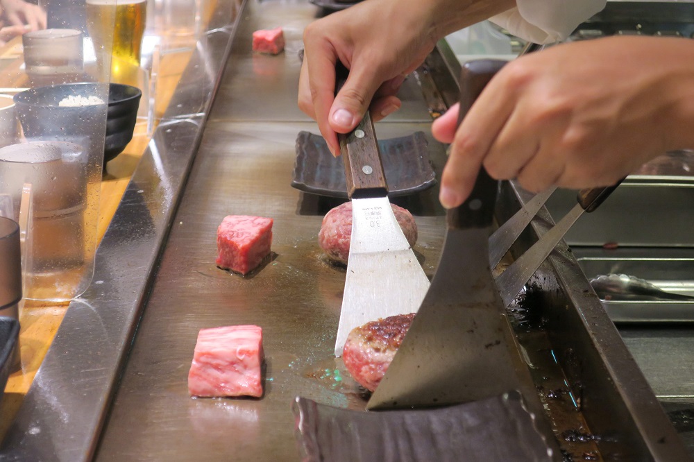 カウンターの中の調理スタッフがお客の前でハンバーグや肉の表面に焼き目を付ける